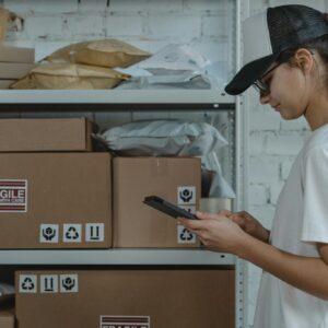 A female courier in uniform managing packages with a device in a storage room.