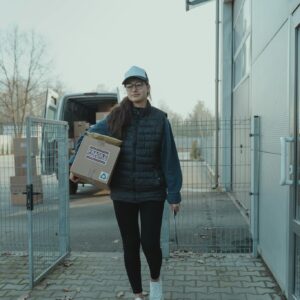 A woman delivering a package in an outdoor setting near a delivery van.