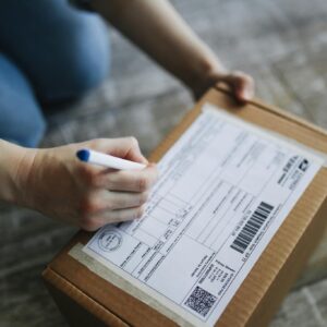 Close-up view of hands writing on a shipping box indoors.