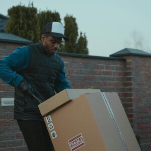 Courier loading cardboard box into a van outdoors, showcasing logistics work.